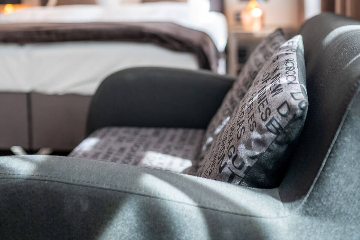 A hotel room with a bed, a nightstand, and a sofa with patterned cushions.