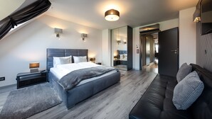 A modern bedroom with a large bed, a dark sofa, and a walk-in closet. - Aparthotel New Lux (Wroclaw)