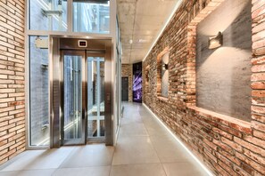 A modern hallway with a brick wall, a glass elevator, and a light fixture. - Aparthotel New Lux (Wroclaw)