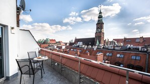 A balcony with a table and chairs, overlooking a cityscape with a prominent clock tower. - Aparthotel New Lux (Wroclaw)
