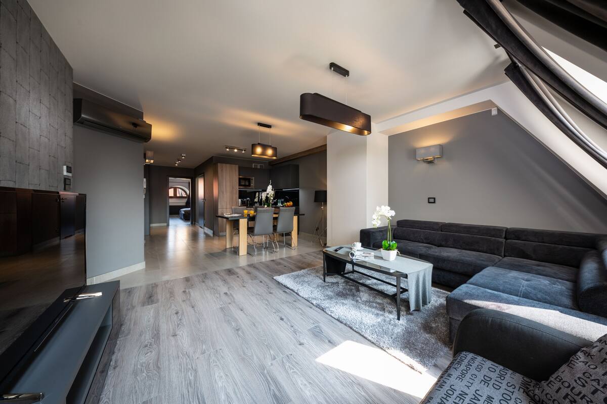 A modern living room with a dark sofa, a coffee table, and a dining area in the background.