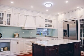 Modern kitchen with a central island, stainless steel refrigerator, and coffee maker.