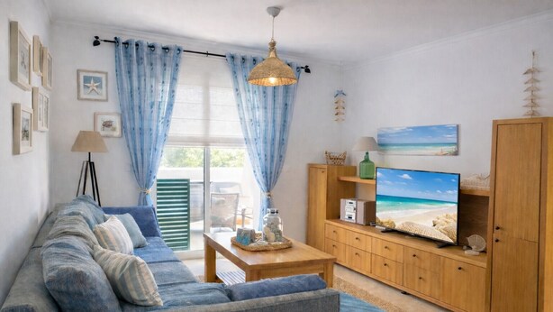 Een woonkamer met een bank, tv, houten kast en uitzicht op het strand door het raam.