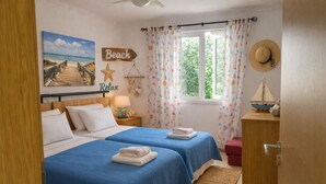 Slaapkamer met twee bedden, een houten hoofdbord, een schilderij met strandthema, een zeester decoratie en een raam met gordijnen.