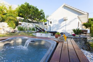 A hot tub with a wooden deck, surrounded by greenery and a stone wall. - Holiday home Mendy with Jacuzzi in the garden in a quiet location above Tučepi (Tučepi)