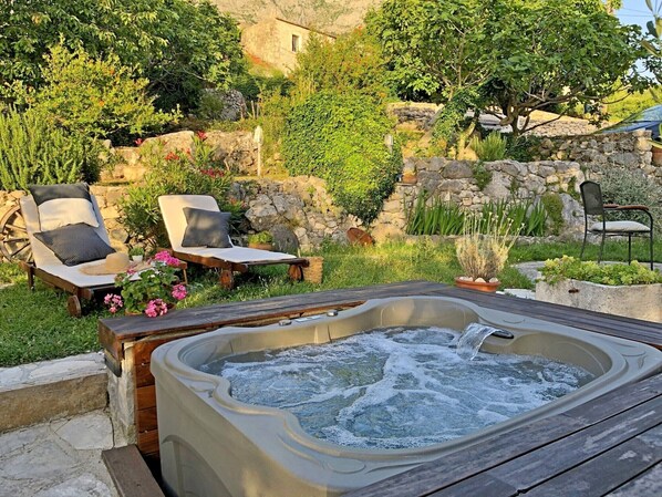 A hot tub surrounded by outdoor seating, a stone wall, and lush greenery. - Holiday home Mendy with Jacuzzi in the garden in a quiet location above Tučepi (Tučepi)