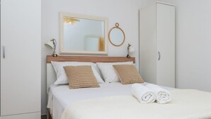 A neatly made bed with white linens and two striped pillows, a wooden headboard, a round mirror, and a white wardrobe. - Holiday home Mendy with Jacuzzi in the garden in a quiet location above Tučepi (Tučepi)
