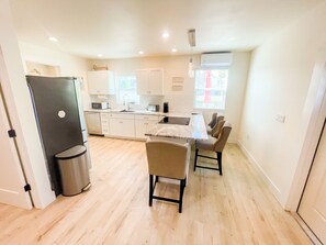 A modern kitchen with white cabinets, a dining area with a table and chairs, and a trash can.