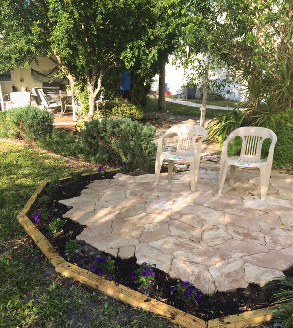 A patio area with stone flooring and two white plastic chairs.