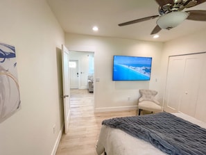 A bedroom with a bed, a ceiling fan, a TV on the wall, and a hallway leading to another room.