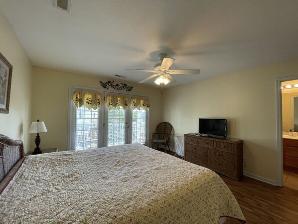 A bedroom with a large bed, a ceiling fan, a dresser, a television, and a chair.