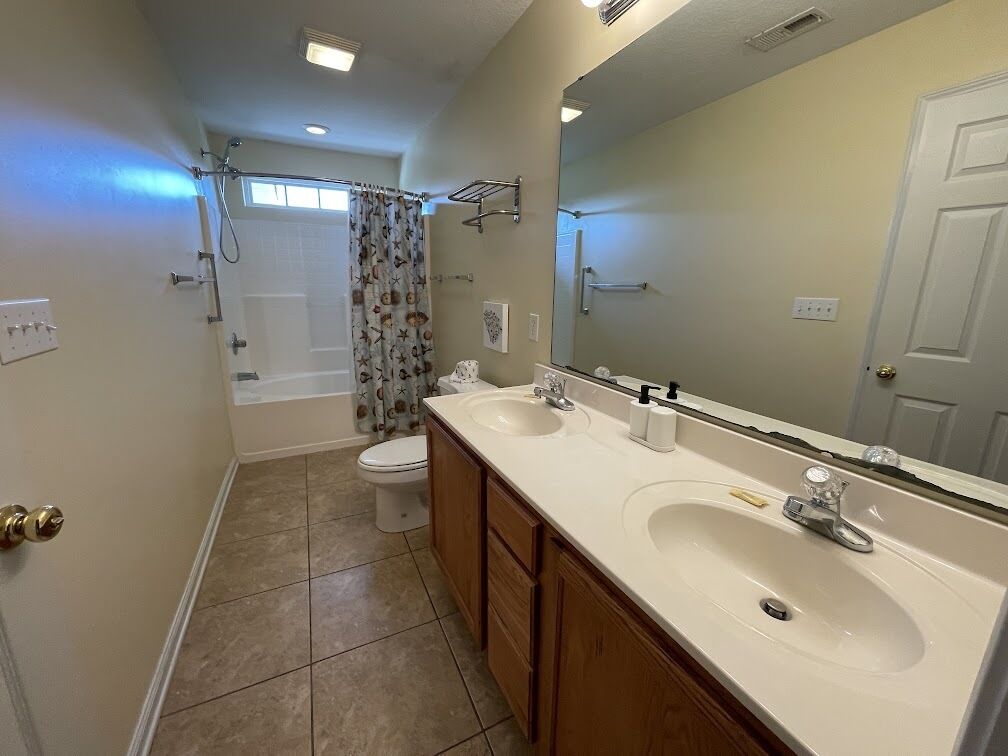 A bathroom with a bathtub, toilet, and a double sink vanity.