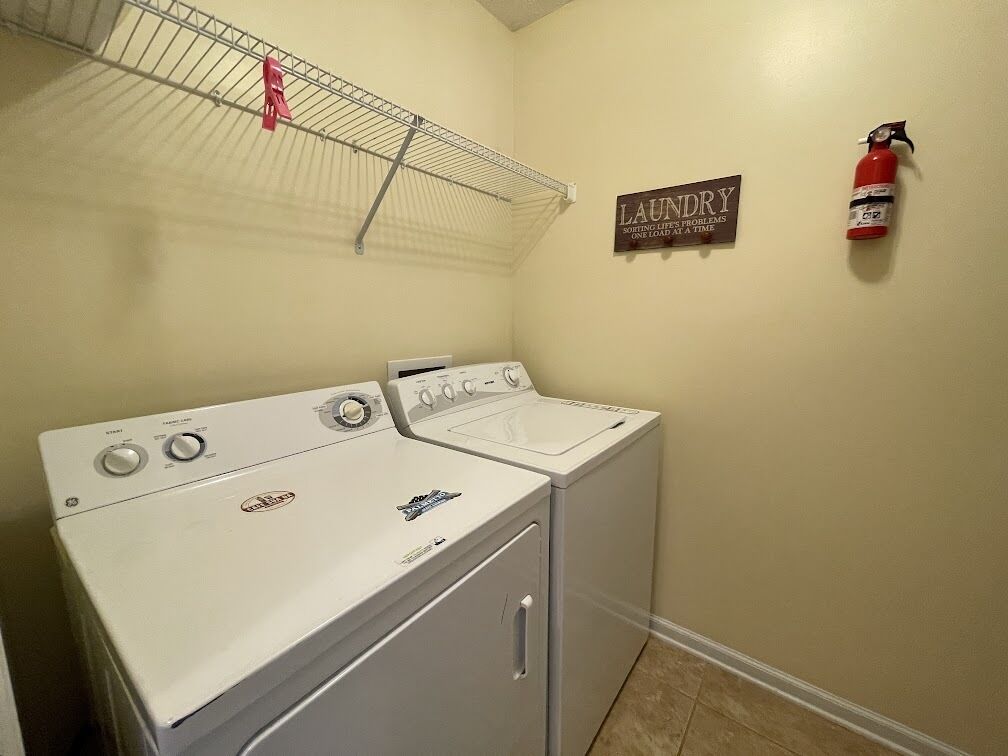 A laundry room with two stacked washers and dryers, a metal drying rack, a fire extinguisher, and a sign that reads "LAUNDRY".