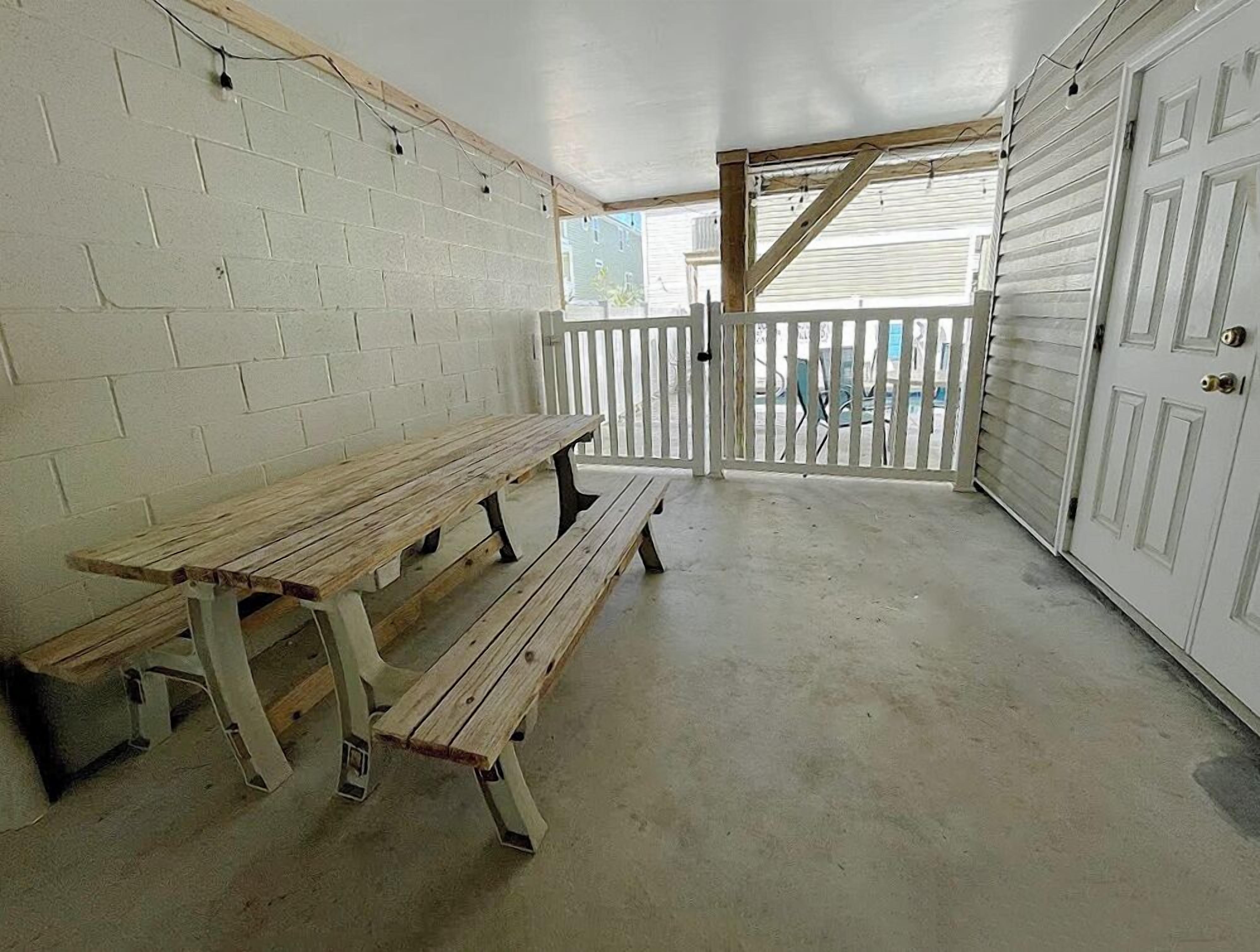 A covered patio area with a wooden bench, white brick walls, and a white door.