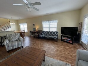 A spacious living room with a wooden floor, a sofa, a coffee table, and a television.