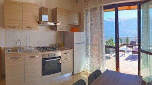 Eine moderne Küche mit Gasherd, Backofen und Kühlschrank, ein Essbereich mit Tisch und Stühlen sowie ein Balkon mit Bergblick.