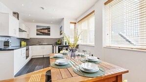 A modern kitchen with white cabinets, a wooden dining table set with plates and glasses, and a view of the outside through large windows. - Seaview Heights | By My Getaways (Brighton)