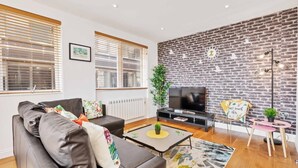 A modern living room with a brick wall, a sofa, a coffee table, a TV, and a small side table with a plant. - Seaview Heights | By My Getaways (Brighton)