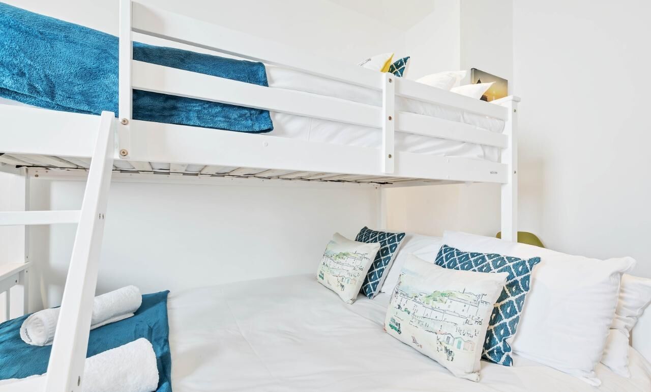 Une chambre avec un lit superpos é, dotée de linge de lit blanc et de touches de couleur bleue, notamment des coussins et une couverture.