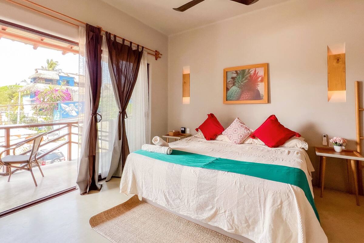 Un dormitorio con cama, ventilador de techo, un cuadro y vistas al exterior.