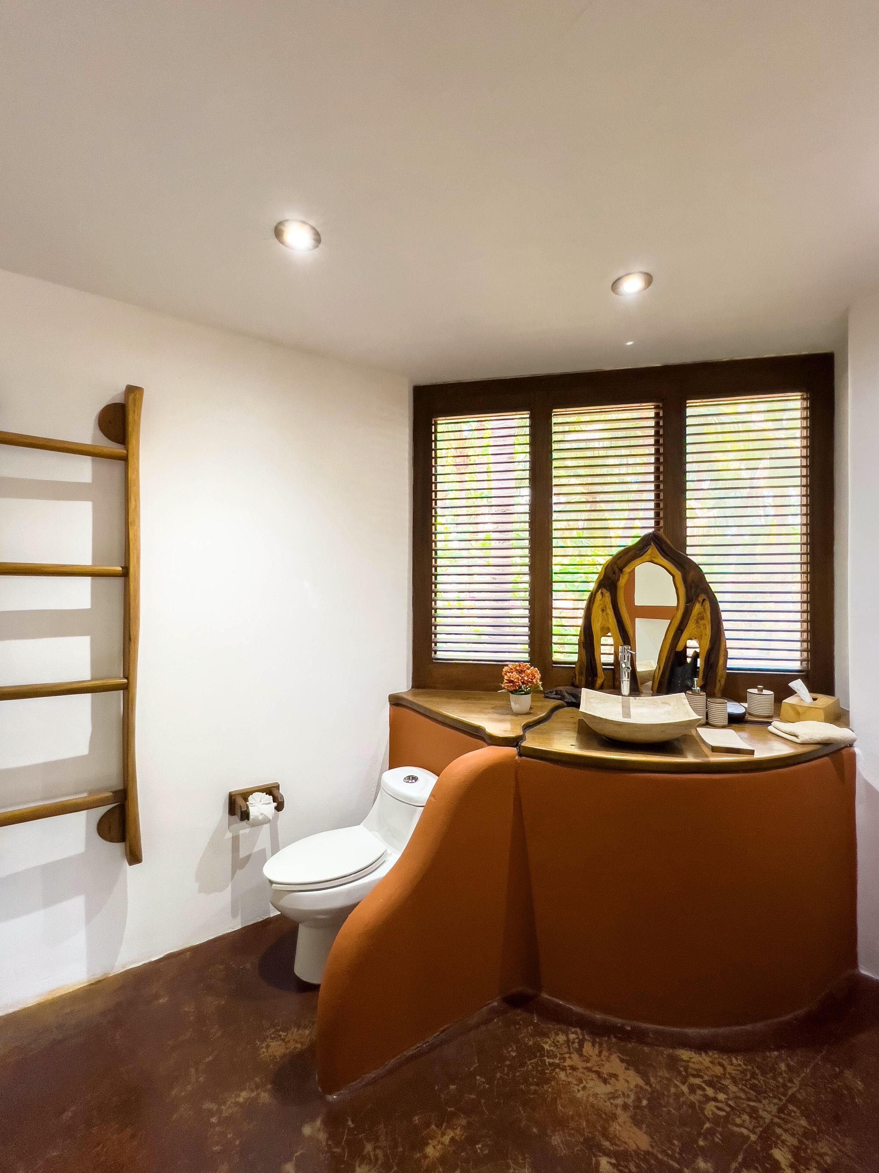 Ein Badezimmer mit Toilette, Waschbecken mit Spiegel und Fenster mit Jalousien.