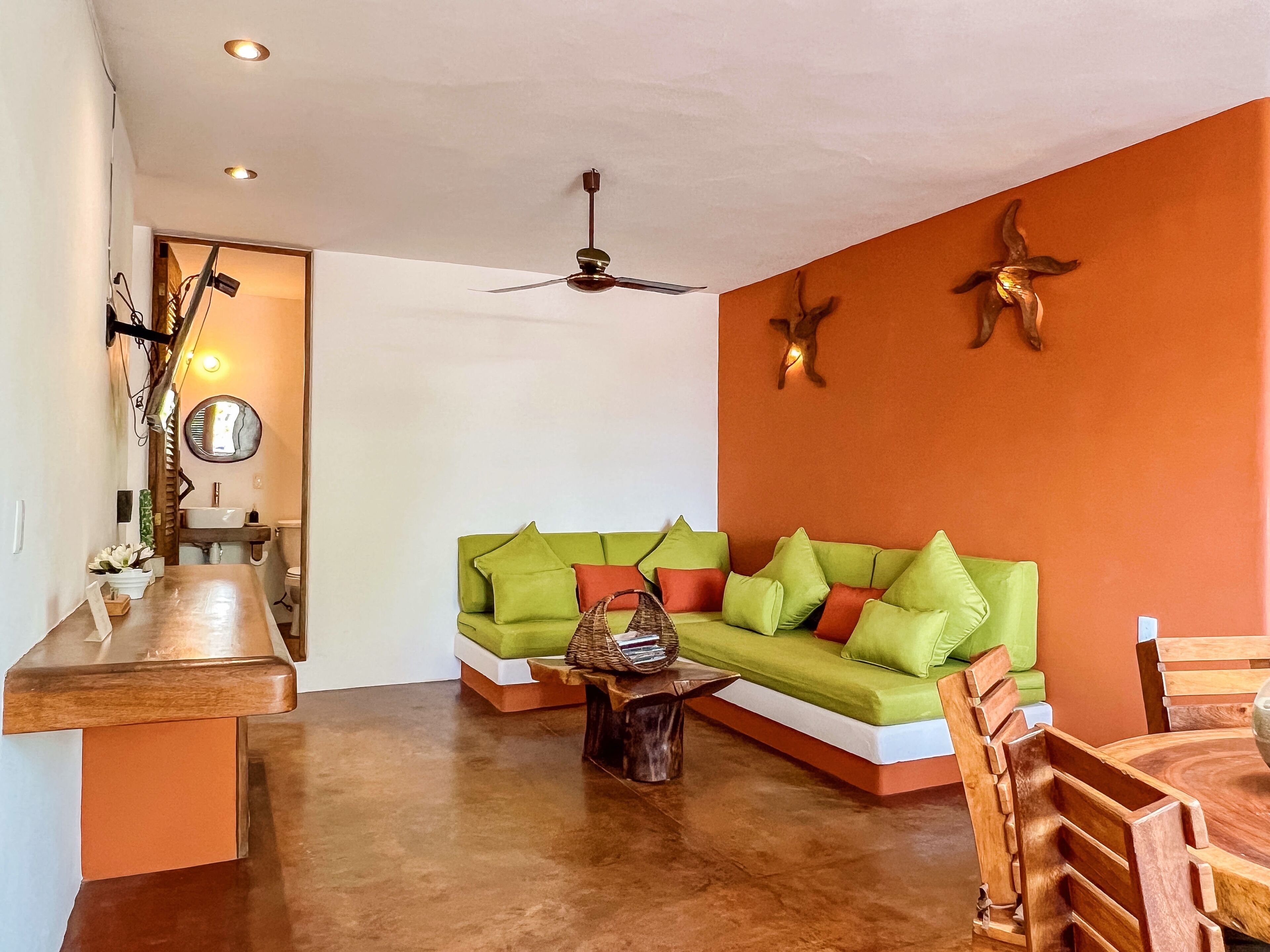 Una sala de estar con un sofá verde, una mesa de centro de madera y paredes anaranjadas.