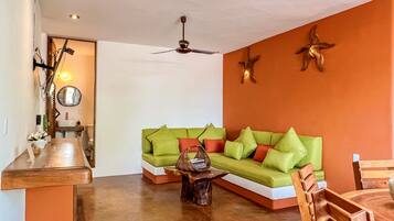 Una sala de estar con un sofá verde, una mesa de centro de madera y paredes anaranjadas.