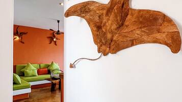 A room with a large, mounted sculpture on the wall, a green sofa with cushions, and a ceiling fan.
