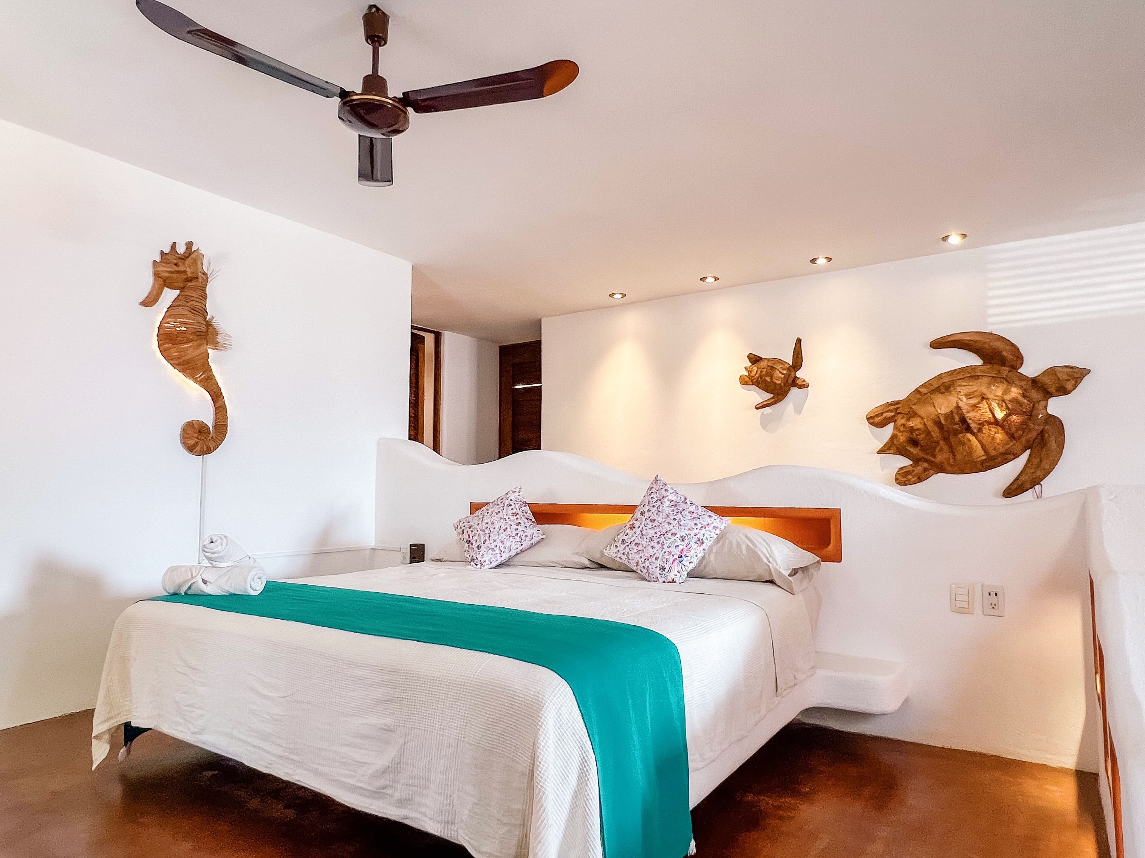 A bedroom with a bed, a ceiling fan, and wall-mounted turtle sculptures.