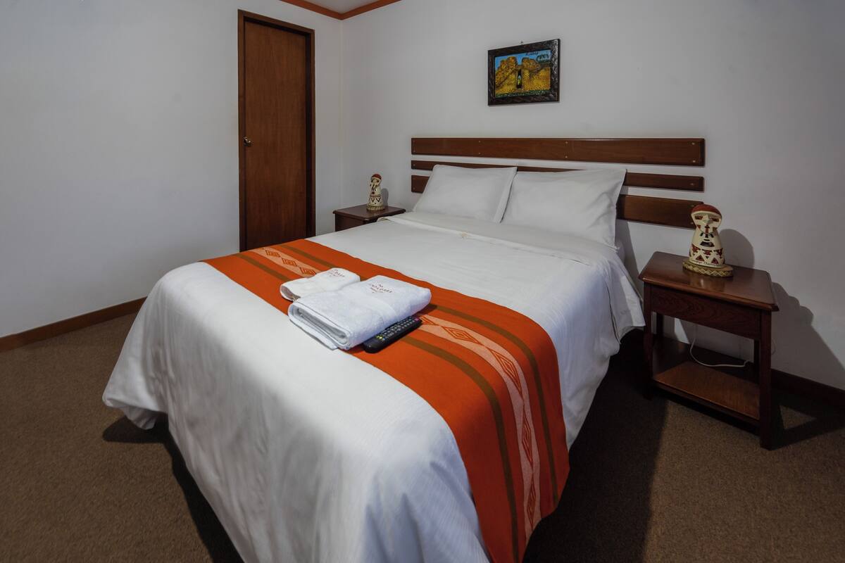 A neatly made bed with a white and orange striped blanket, a wooden headboard, and a small nightstand with a decorative item.