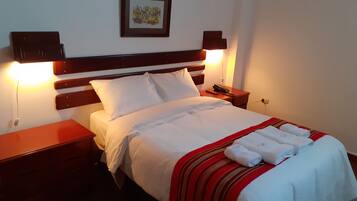 A neatly made bed with white linens and a red-striped blanket, a bedside phone, and a wall-mounted picture frame.