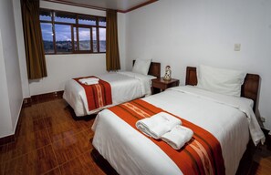 Habitació d'hotel amb dos llits, un sòl de fusta, una tauleta de nit amb una làmpada i una finestra amb vista a una vila.