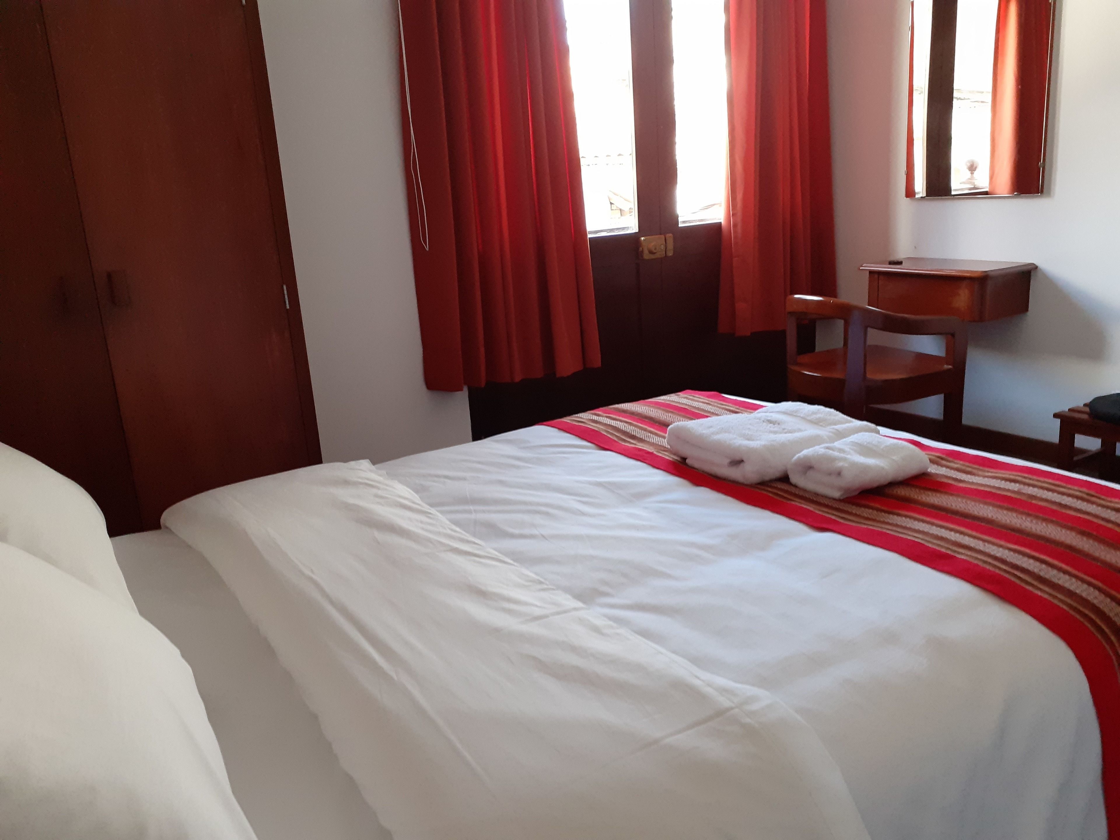 Una habitación de hotel con una cama, una mesita de noche de madera, una silla y una pequeña mesa.