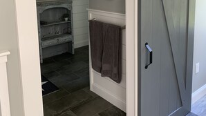 A bathroom with a sliding door, a towel hanging on the wall, a small round mirror, and a rustic vanity with a plant. - Goose Rocks Retreat - relax, refresh, recharge  (Kennebunkport)