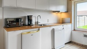 A compact kitchen with white cabinetry, a wooden countertop, a coffee maker, a toaster, a sink, and a dishwasher.