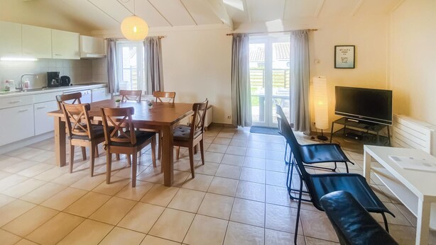 A spacious living area with a dining table, chairs, a TV, and a kitchen area with cabinets and appliances.