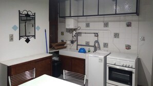 Een kleine keuken met een koelkast, oven en gootsteen. Er staat een kleine prullenbak en een blauwe bak op het aanrecht.