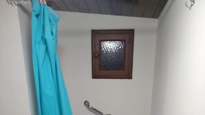 Een kleine badkamer met een bad, douchegordijn, handgreep, raam en een plank met toiletartikelen.