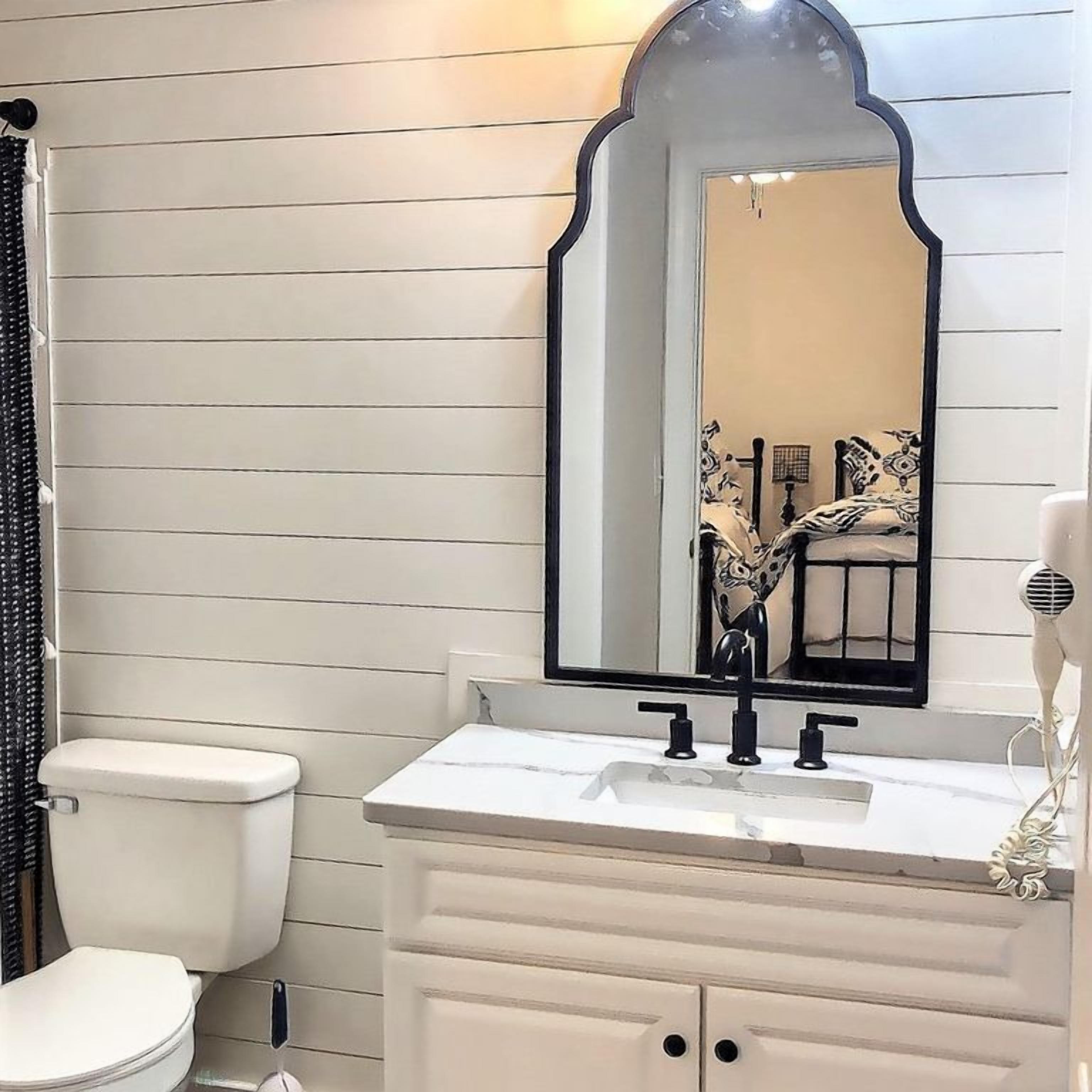 Un baño con tocador blanco, espejo de marco negro y retrete.