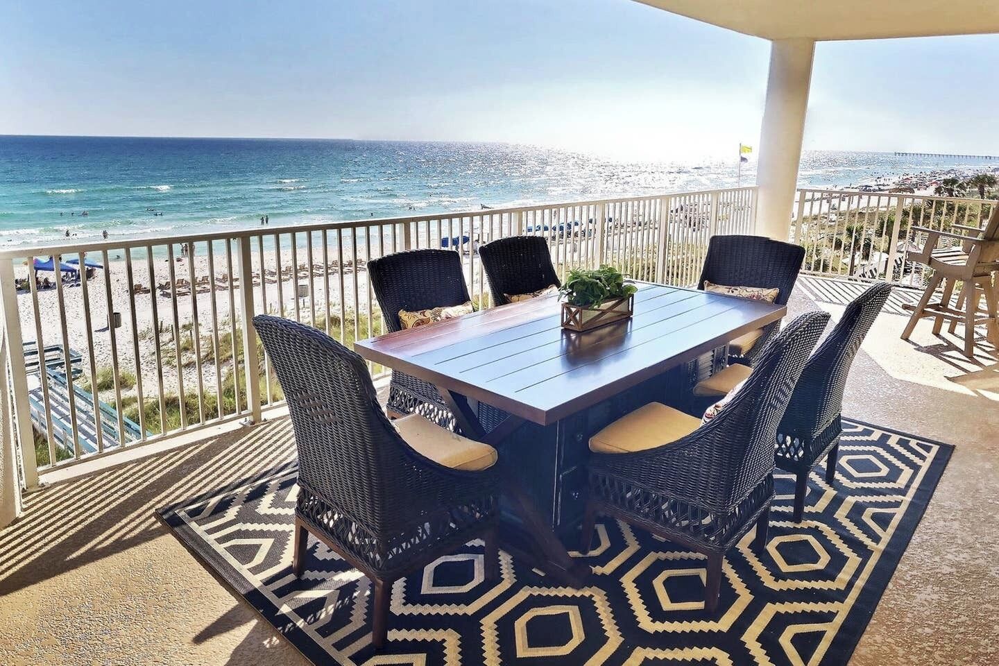 A terrace with a table and chairs overlooking a beach.