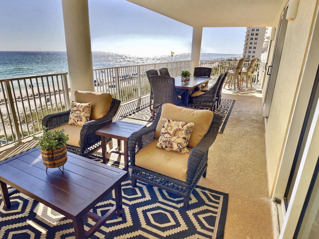 A balcony with wicker furniture, a patterned rug, and a view of the ocean.