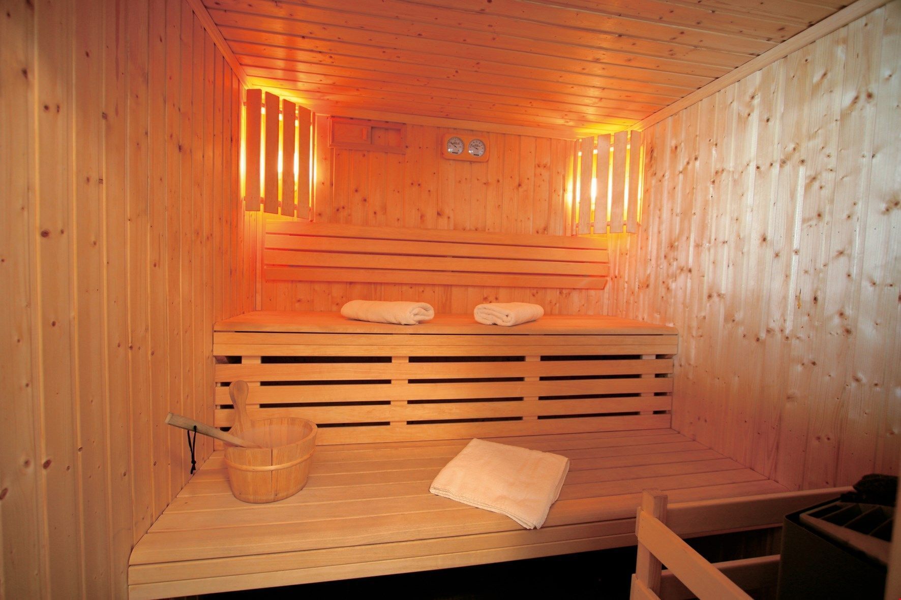 A wooden sauna with benches, a wooden bucket, and a towel on the floor.
