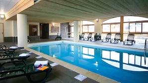 Une piscine intérieure dotée de chaises longues et d’un plafond en bois.