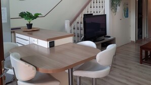 A modern kitchen with a wooden island, white bar stools, a dining table, a TV, and a staircase leading to a balcony. - 70 m² modern house, 650 m from the beach, rated 3 stars. 2027 RATES OK (Fleury)
