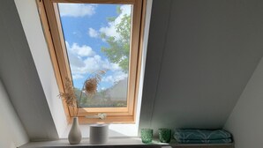 A skylight with a view of trees and sky, a vase, and two green cups on a shelf.
