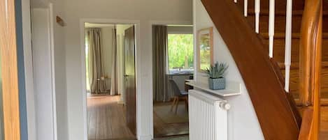Una escalera conduce a una habitación con escritorio y silla, un radiador y vistas de un jardín a través de una ventana.