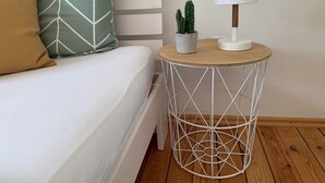 A neatly made bed with patterned pillows, a small potted cactus, and a white lamp on a round metal table beside the bed.