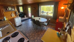 A cabin interior with a kitchen, dining area, and a window with a view of the outdoors. - Entire Cabin: Step Back in Time at The Piney Lodge (Grand Lake)