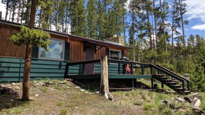 A cabin with a wooden exterior, a porch, and a staircase leading to a deck. - Entire Cabin: Step Back in Time at The Piney Lodge (Grand Lake)