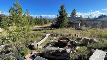 An outdoor area with a fire pit, wooden logs, and a metal chair.